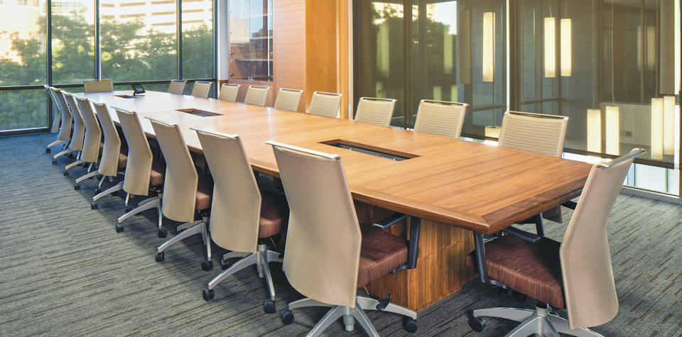 Conference table featuring Walnut veneers, solid Walnut edging, integrated electrical outlets, and Walnut veneered pedestal bases.